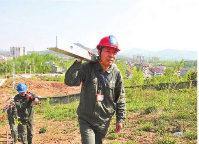 曾凡平扛着施工材料上山,架设超高压输电线路