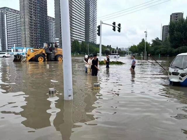 ▲2021年7月21日，在郑州一号线博学路地铁站附近，几位年轻人互相扶助在水中前行。新京报记者涂重航摄