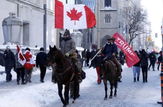 ·骑马在渥太华街头招摇过市的“自由车队”支持者，其中一人高举支持美国前总统特朗普的旗子。