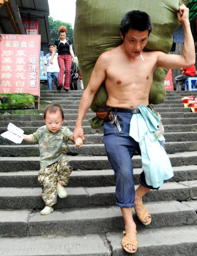 ▲2010年6月20日，摄影师许康平在重庆朝天门码头拍下冉光辉牵着儿子扛货的照片。许康平供图
