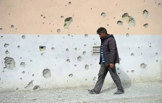 ▲2020年9月29日，在阿塞拜疆邻近纳卡边境的塔塔尔地区，一名村民从布满弹孔的墙壁旁经过。图/新华社