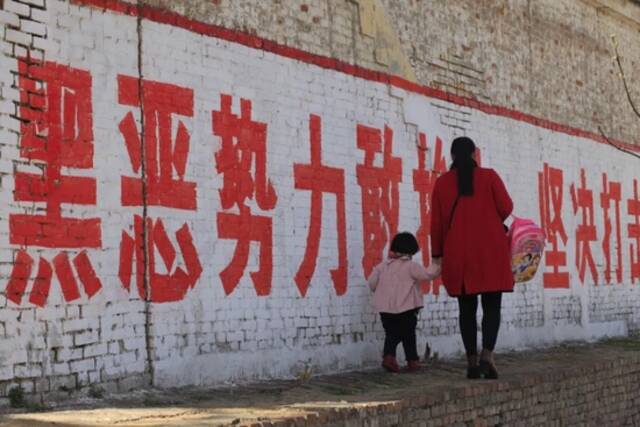 2018年4月7日，河南安阳，一名妇女拉着孩子在标语前走过。