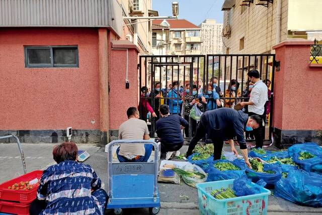 3月16日，在上海的一些临时封闭管控小区，快递小哥将包裹送到小区门口，菜贩则通过小区围栏向居民售卖食品。图/澎湃影像