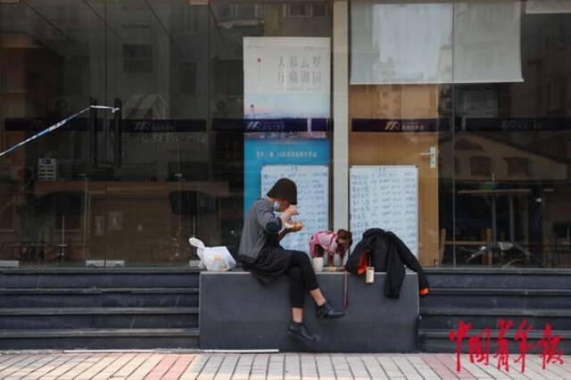 5月3日，上海市黄浦区，“电话亭女士”与她的狗“丽丽”正在一家暂停营业的房屋中介门前吃午饭。中青报·中青网记者李强/摄