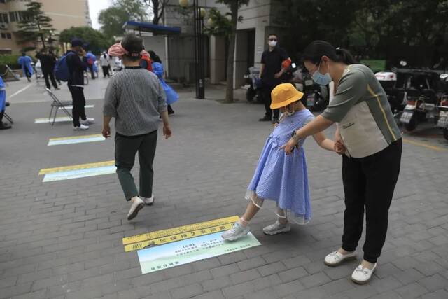 ▲5月5日，海淀区羊坊店街道莲花小区，一位检测完核酸的妈妈带着女儿在读地上的古诗。新京报记者浦峰摄