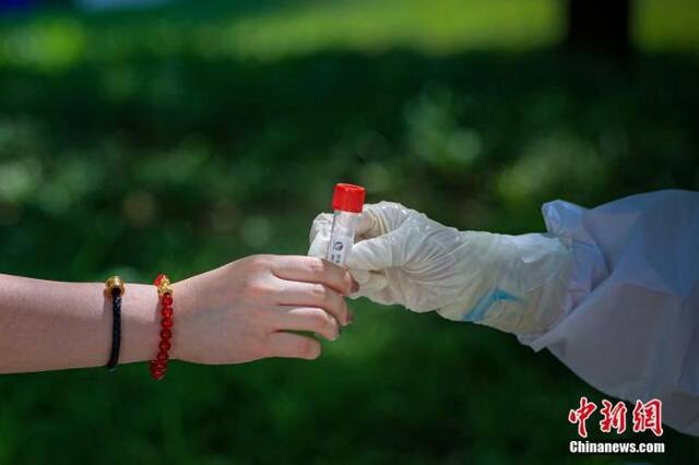 图为5月22日，一位北京市民将自己的病毒采样管交给采样人员。中新社记者贾天勇摄