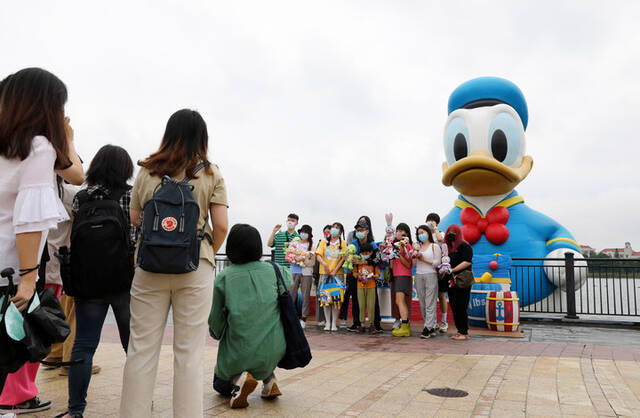 6月10日，游客在上海迪士尼度假区内的星愿湖边与唐老鸭造型的充气玩偶合影。新华社记者方喆摄