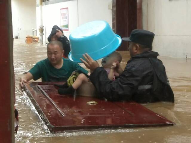 暴雨中，孙建军用脸盆为孩子挡雨。受访者供图