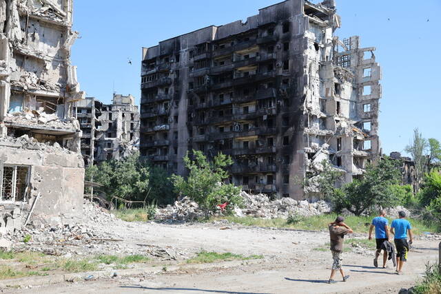 ↑6月18日，当地居民从马里乌波尔的受损建筑旁走过。新华社发（维克托摄）
