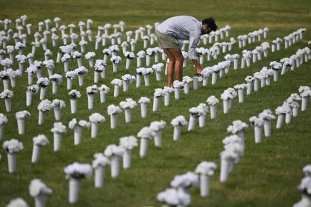 ▲6月8日，一名男子在华盛顿调整白色花瓶，每一个花瓶象征2020年死于枪击的每一个美国人。（法新社）