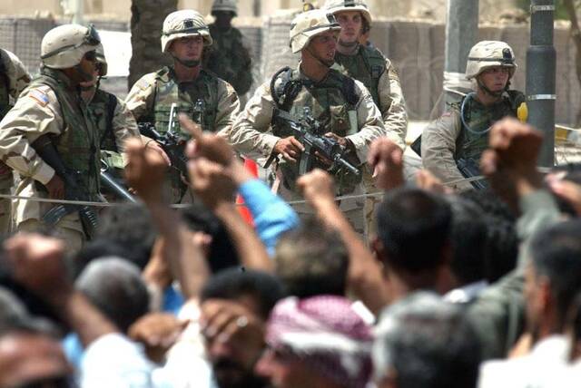 这是2003年6月18日，美军士兵在伊拉克首都巴格达美英联军临时总部门前持枪面对数百名示威的伊拉克人。
