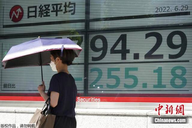 6月29日，一名戴口罩的人走在显示日本日经指数的电子股票板前。