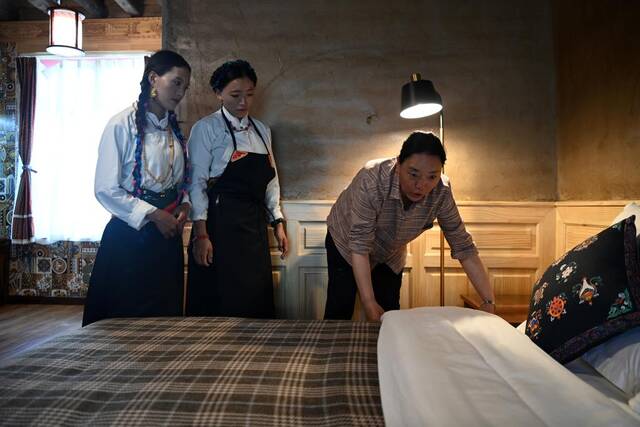 7月16日，才卓玛（右一）给山庄工作人员演示床品整理。新华社记者范培珅摄