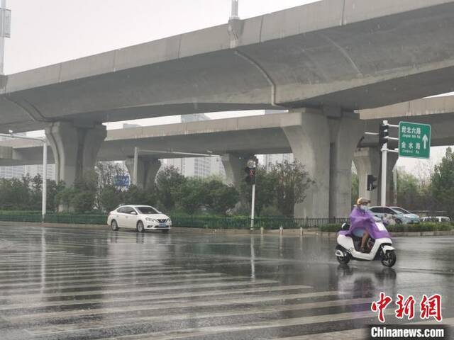 图为7月15日，郑州市区降雨，市民着雨衣出行。刘鹏摄