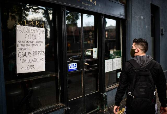 阿根廷布宜诺斯艾利斯，一名男子走过一家关门的餐馆，招牌上写着:“亲爱的邻居和客户们，隔离80天，我们难以维持。”图源视觉中国
