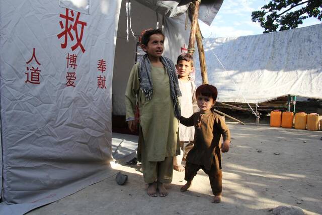 7月18日，在阿富汗地震重灾区帕克提卡省齐鲁克区，孩子们站在中国红十字会援助的救灾帐篷外。新华社发（萨巴文摄）