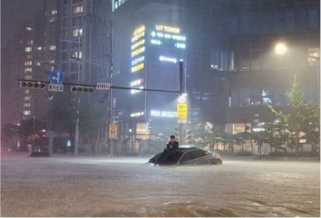 8日当晚，在首尔瑞草区某公寓前,一名男子爬上被水淹没的车辆以防自己也被雨水淹没。图自韩媒
