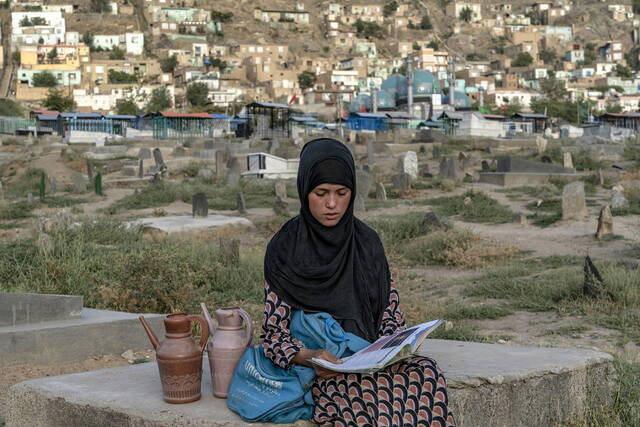 当地时间2022年7月30日，阿富汗首都喀布尔，14岁的阿富汗女孩Sara坐在墓地边看书边等待顾客买水。视觉中国图