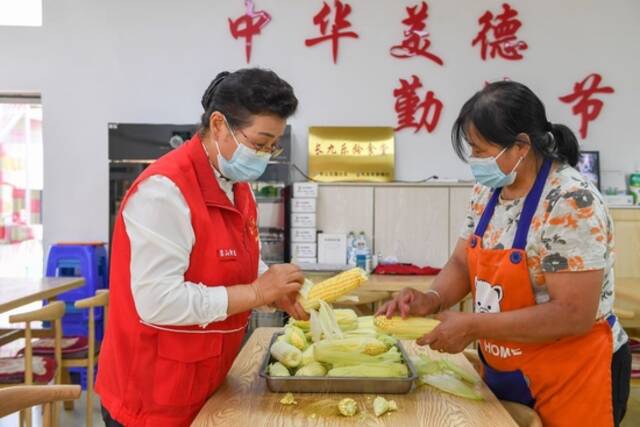 8月24日，在团山街道长山花园社区食堂，吴亚琴（左）与志愿者房桂香一同剥玉米。新华社记者张楠摄