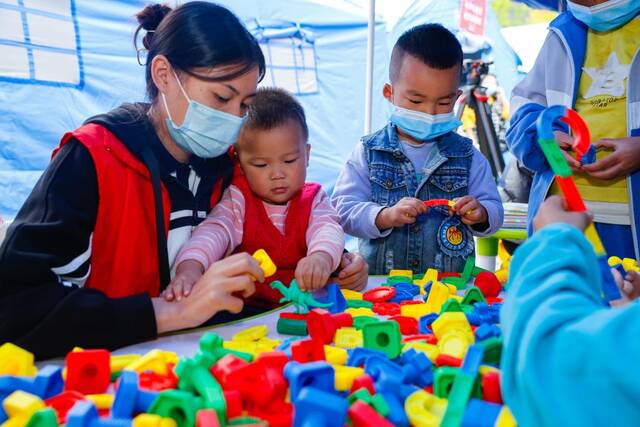 9月7日，在四川省甘孜州泸定县磨西镇地震救灾安置点，志愿者陪伴孩子们在青青儿童乐园玩耍。新华社记者沈伯韩摄