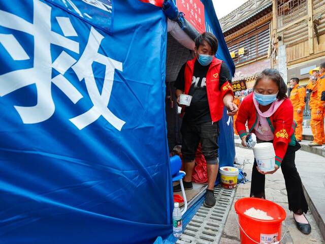 9月7日，在四川省甘孜州泸定县磨西镇的地震灾后安置点，志愿者在为人们分发米饭。新华社记者沈伯韩摄