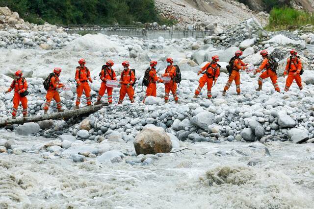 9月8日，在四川省甘孜州泸定县磨西镇附近，救援人员站在临时架设的小桥上向河对岸的村民运送生活物资。新华社记者沈伯韩摄