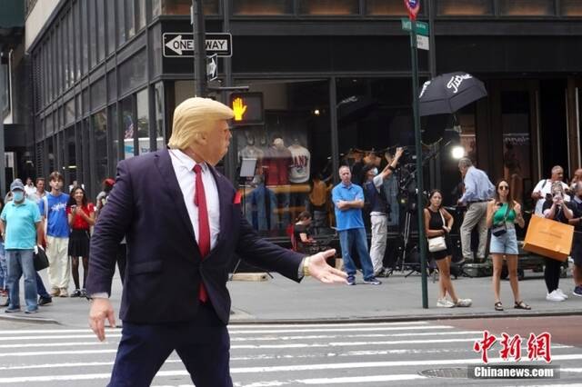 资料图：当地时间8月10日，一名戴着面具的示威者在美国纽约特朗普大厦外模仿美国前总统特朗普。近两日，特朗普大厦前示威者、记者、围观民众等人流聚集。中新社记者廖攀摄