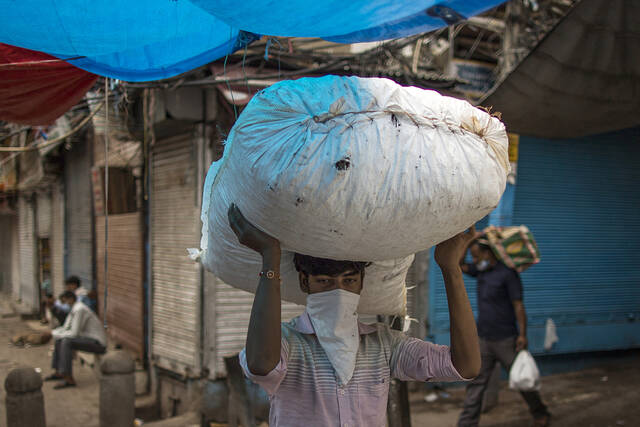 当地时间2020年8月31日，印度新德里，戴着口罩的搬运工头上顶着一个袋子。人民视觉资料图