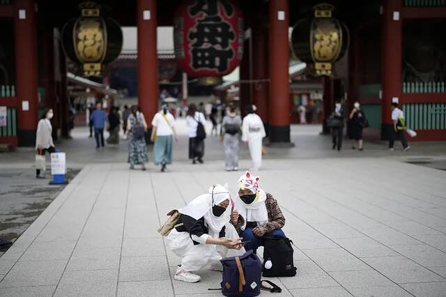 当地时间2022年6月10日，日本东京浅草区一条购物街上，外国游客戴着防护口罩自拍。图/视觉中国