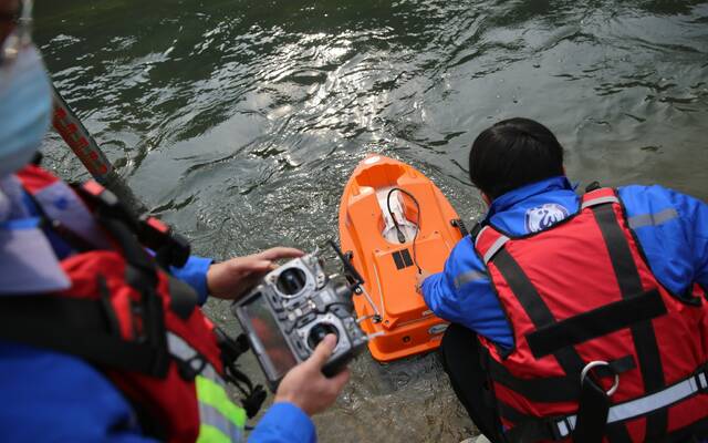 郭新与刘晏涛将搭载声学多普勒测流剖面仪的遥控船放入河道。新京报记者郑新洽摄