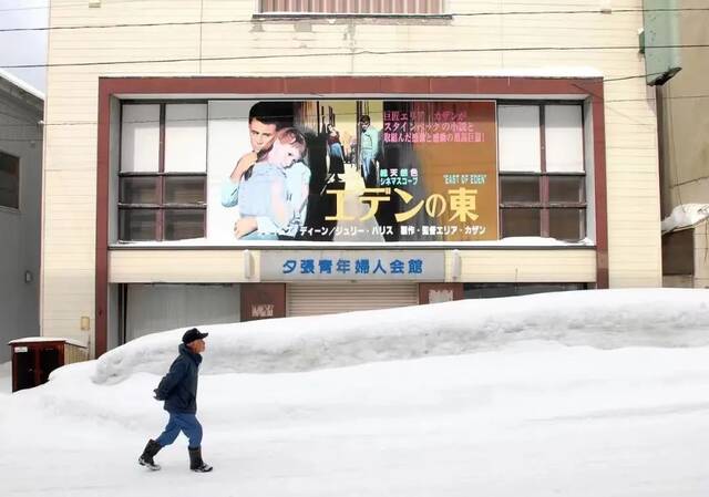 2007年3月13日，日本夕张，一位居民雪天走过一栋挂着电影海报的废弃会馆。夕张年均气温低于6℃，一年有一半时间被雪覆盖（视觉中国供图）