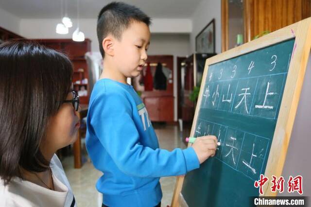 资料图：甘肃兰州市七里河区王家堡小学学生芮明亮在家给家长讲解汉字笔画，这也是他的寒假作业之一。艾庆龙摄