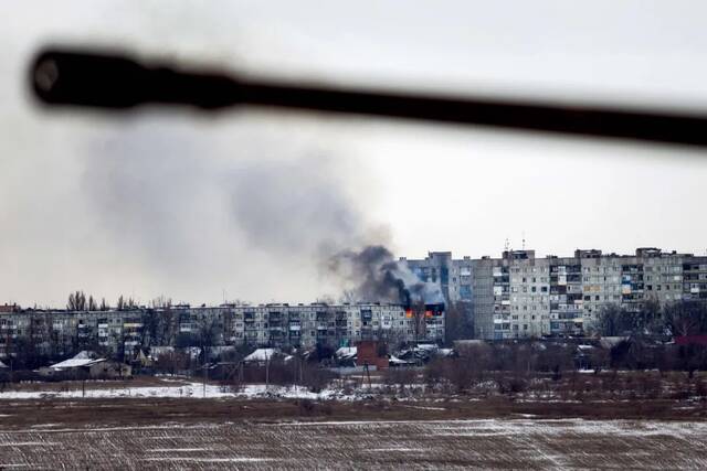 2月14日，顿涅茨克地区巴赫穆特，一辆乌克兰军车驶过被俄罗斯炮火击中的公寓楼。图/视觉中国