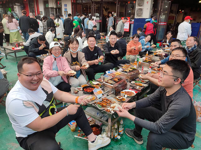 2023年3月31日，山东淄博，食客们围炉吃烧烤，展示淄博烧烤“小饼包一切”的独特吃法。视觉中国图