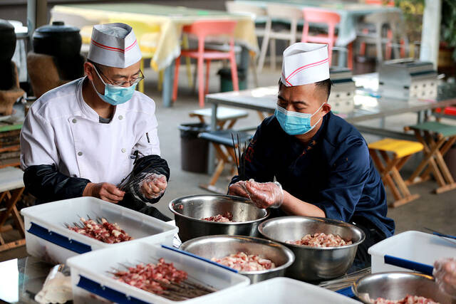 2023年3月31日，山东淄博，一家烧烤店的厨师忙着串肉串。视觉中国图
