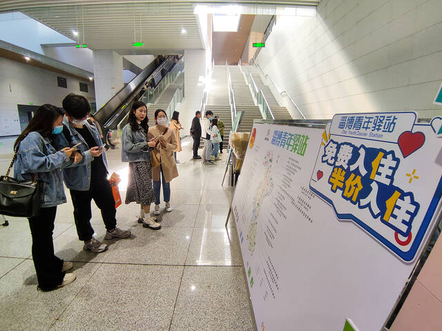 2023年4月2日，山东淄博，淄博站内，游客们查看青年驿站的惠游政策。视觉中国图