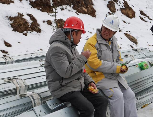 腊巴山风电建设现场，李现臣（右）在雪地里边吃简餐边交流工作。受访者供图
