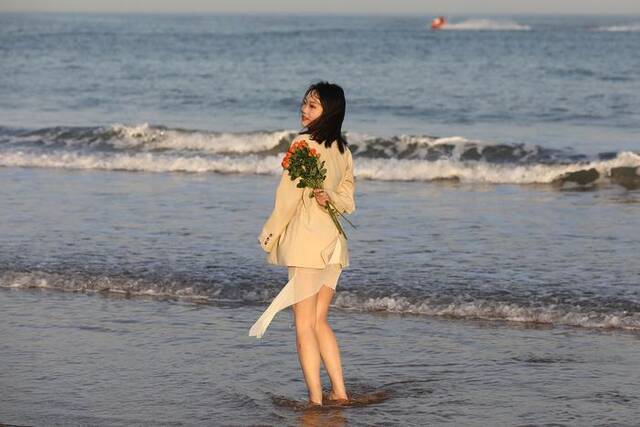 5月8日，青岛石老人海水浴场海边，游客穿夏装游玩、拍照。