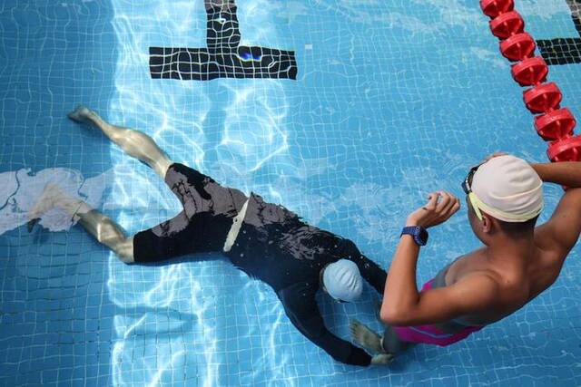 6月12日，陈勋虎（左）在游泳池帮儿子的腿绑弹力带来调整游泳姿势。新华社记者张丽芸摄