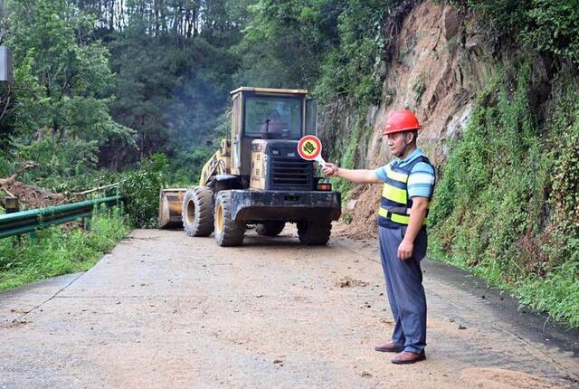 7月9日，在太湖县牛镇镇天桥村天天公路一段山体垮塌处，王和松示意车辆暂停通过。