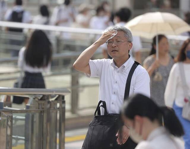 当地时间2023年7月12日，日本东京街头，人们一边在烈日下行走，一边擦汗。
