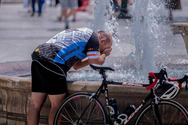 当地时间2023年7月12日，希腊雅典，高温天气下，一名骑自行车的人在市中心的一个喷泉旁洗脸降温。