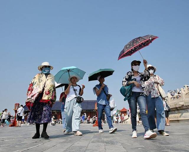 2023年7月19日，北京天坛公园祈年殿前人头攒动，游客在烈日炙烤中撑伞游览兴致不减。视觉中国图