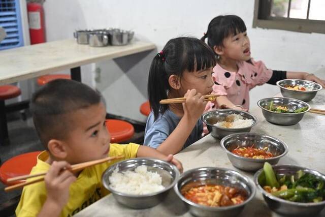 7月27日，在福建省泉州市安溪县蓬莱镇安溪八中安置点，三位小朋友在食堂吃晚饭。新华社记者周义摄