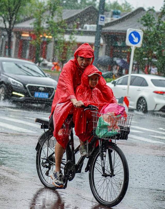 7月30日，大人带着小孩在雍和宫大街冒雨骑行。新华社记者陈钟昊摄