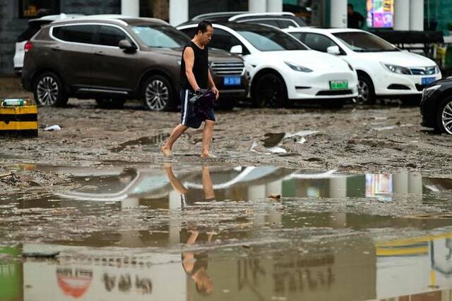 7月31日，北京门头沟区，一名男子提着鞋走在布满积水和泥浆的街道上。