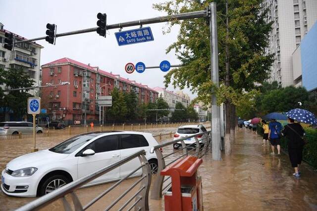 7月31日，在门头沟区大峪南路，行人从积水的路面和泡水的车辆旁走过。新华社记者鞠焕宗摄