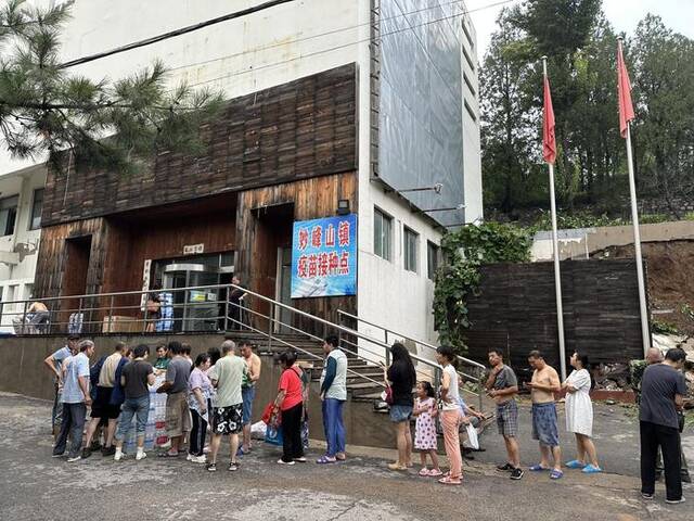 安置点为一栋四层高的白色外墙建筑，村民正在排队领取物资。新京报记者涂重航摄