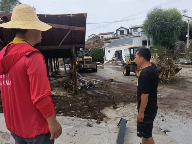 8月4日早晨，雁翅镇田庄村支书崔春洪（左），在村口组织清理洪水留下的砂石、树木、车辆。新京报记者周怀宗摄