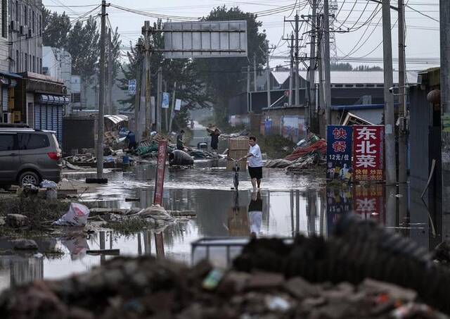 8月5日，河北涿州，一男子骑着自行车，扛着从当地一家企业打捞上来的货物箱，艰难地穿过退去的洪水。